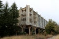 Cold War era abandoned hotel complex with destroyed facade and windows on top of small hill surrounded with tall trees