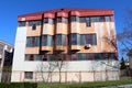 Cold war style large industrial building with dilapidated facade behind metal fence and trees without leaves