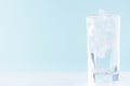 Cold water with ice in misted drinking glass on soft light blue background, white wood board. Royalty Free Stock Photo