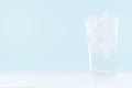 Cold water with ice in misted drinking glass on soft light blue background, white wood board. Royalty Free Stock Photo