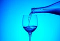 Cold water pouring into the glass from the glass bottle on a blue background. Royalty Free Stock Photo
