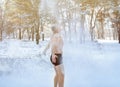 Cold weather training, winter fun. Mature man in underwear standing under falling snow, throwing it at himself in park