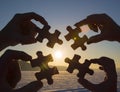 Collaborate four hands trying to connect a puzzle piece with a sunset background. Royalty Free Stock Photo
