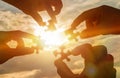 Collaborate four hands trying to connect a puzzle piece with a sunset background. A puzzle in hand against sunlight. Royalty Free Stock Photo