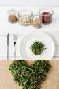 Collage of fresh microgreen on plate with cutlery, heart of microgreen on sackcloth and glass jars with superfood Royalty Free Stock Photo