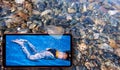 Collage of sunny jellyfish floating in water above Black sea stones and cell phone displaying tanned girls in bikini on screen