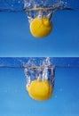 Whole lemon dropped in water against gradient blue background