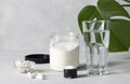 Collagen powder in a jar and measuring spoon, collagen capsules and a glass of water on a gray background with monstera