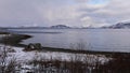 Collapsed old wooden shed at the shore of Altafjord, Norway with bare trees and snow-covered mountains on cloudy day in winter. Royalty Free Stock Photo