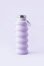 Collapsible reusable lilac water bottle on purple background. Sustainability eco-friendly lifestyle