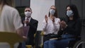 Colleagues in coronavirus face masks clapping in slow motion as spokesperson presenting business report on Covid-19