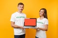 Colleagues couple in white t-shirt inscription volunteer hold laptop pc computer, blank empty screen isolated on yellow Royalty Free Stock Photo