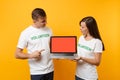 Colleagues couple in white t-shirt inscription volunteer hold laptop pc computer, blank empty screen isolated on yellow Royalty Free Stock Photo