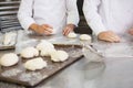 Colleagues kneading uncooked dough on worktop