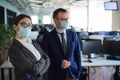 Colleagues in protective masks work in an open space office. A man and a woman in suits work at the workplace. Head and