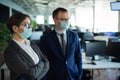 Colleagues in protective masks work in an open space office. A man and a woman in suits work at the workplace. Head and