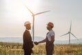 Colleagues shaking hands with wind turbines on background