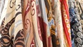 A variety of batik fabrics with intricate patterns and vibrant colors hanging vertically