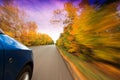 A car on curvy autumn forest road, with motion blur from its speed