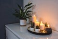 collection of burning decorative candles on a white wooden shelf with a green house plant modern warm design