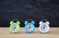 A collection of colorful alarm clocks over wooden desk in front of blackboard. Royalty Free Stock Photo