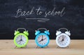 A collection of colorful alarm clocks over wooden desk in front of blackboard.