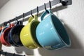 A collection of colorful mugs hanging on black hooks against a white wall Royalty Free Stock Photo