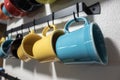 A collection of colorful mugs hanging on black hooks against a white wall Royalty Free Stock Photo