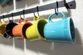 A collection of colorful mugs hanging on black hooks against a white wall Royalty Free Stock Photo