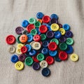 A collection of multicolored plastic buttons scattered on a textured beige fabric Royalty Free Stock Photo