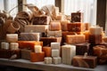 A collection of natural, handmade soaps in various sizes and shades of brown and cream are arranged against a window