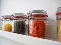 Collection of rustic glass jars filled with dry food such as red gluten free lentil pasta and black lentils on a white shelf