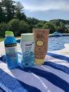 Collection of sunscreen bottles next to an inground pool on a sunny day