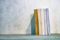 a collection of thick books neatly arranged standing on a table against a white wall background