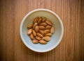 Collection Wet soaked almonds in a plastic bowl kept on a textured wooden base.