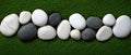 A collection of white, black, and gray stones arranged in a row on a green surface. Royalty Free Stock Photo