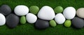 A collection of white, black, and green pebbles arranged in a row on a green surface. Royalty Free Stock Photo