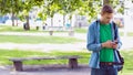 Man standing under leafy tree shade in urban park, checking smartphone beside wooden bench Royalty Free Stock Photo