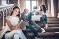 College life.A beautiful young student sitting on stairs in campus using the tablet while her friends work with laptop Royalty Free Stock Photo