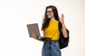 College student girl on gray background, smiling at camera, pressing laptop to chest, wearing backpack, ready to go to studies, Royalty Free Stock Photo