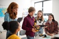 College student presenting his builded robotic toy to young science teacher and his schoolmates at robotics classroom at