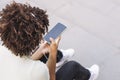 College student sitting on the stairs working on a laptop.Young curly woman recording an audio message through her smartphone, Royalty Free Stock Photo