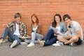 College students sitting ground by brick wall