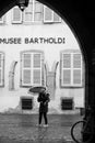 Woman walking in the street with umbrella in front of the Bartholdi museum