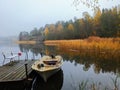 Colofrul autumn landscape with wooden pier, boat in the still water and forest trees reflection on the background Royalty Free Stock Photo