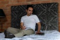 Colombian man sitting on his bed writing in a notebook and checking his laptop Royalty Free Stock Photo