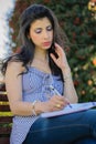 Colombian woman with sunglasses sitting on a garden bench writing in her notebook Royalty Free Stock Photo