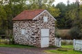 Colonial stone spring house with wooden shutters by white garden gate. Royalty Free Stock Photo