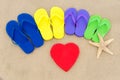 Color flip flops and heart on sandy beach