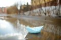 Color origami paper boat in large puddle on street near town houses. Paper ship floating in water. Activities for kids in early